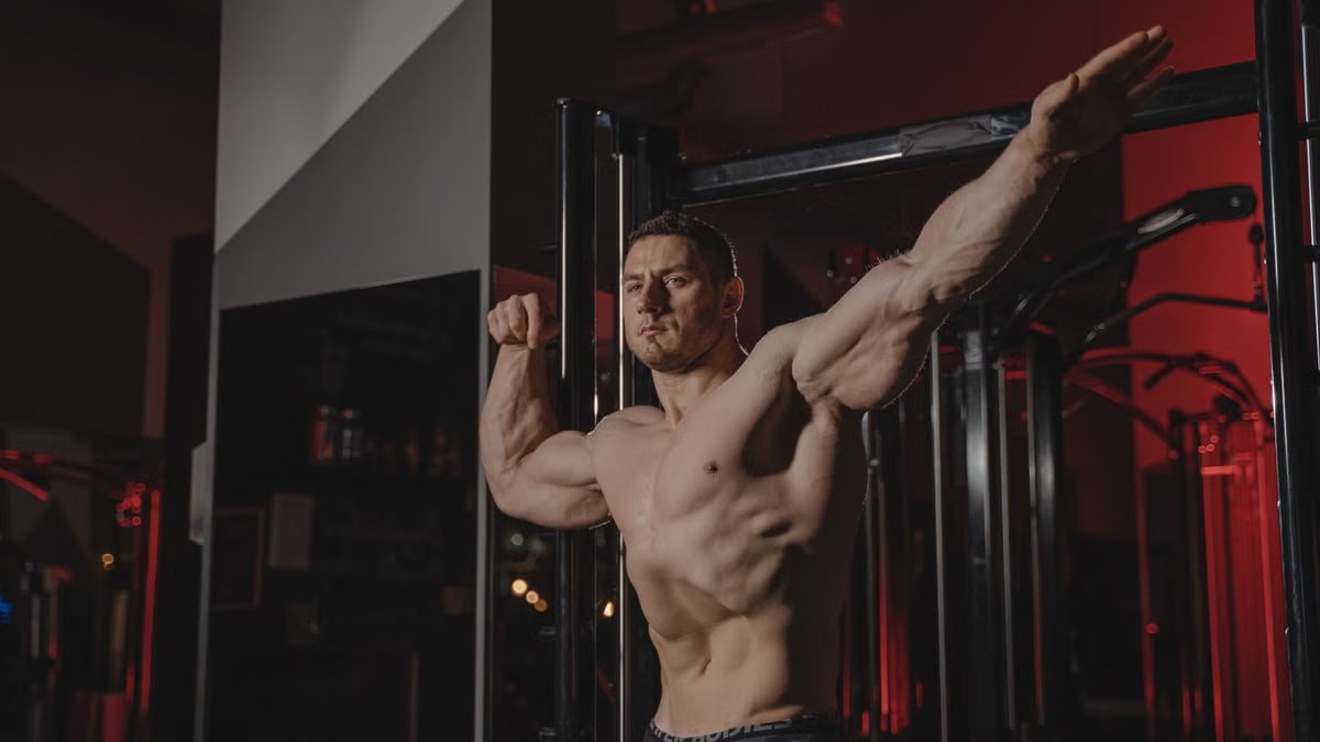 Strong and muscular man posing topless in a gym, showcasing fitness and strength.